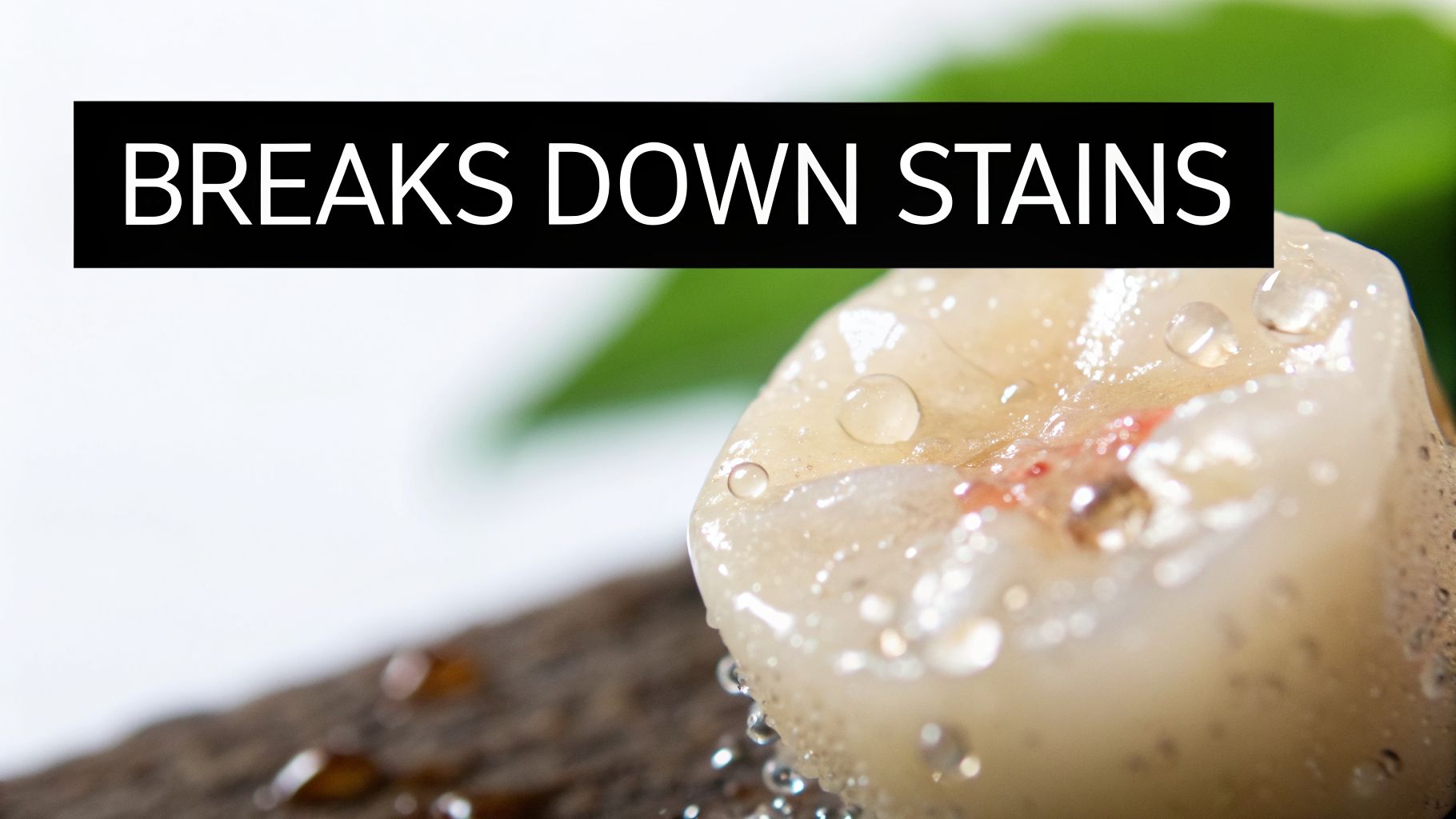 A close-up of a stained tooth covered in water droplets with the text 'BREAKS DOWN STAINS'.