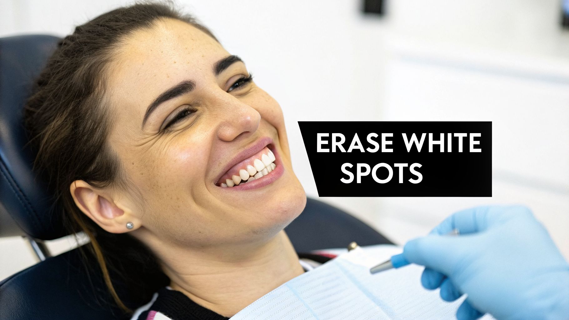 A smiling woman in a dental chair with a gloved hand holding a dental tool. Text: ERASE WHITE SPOTS.