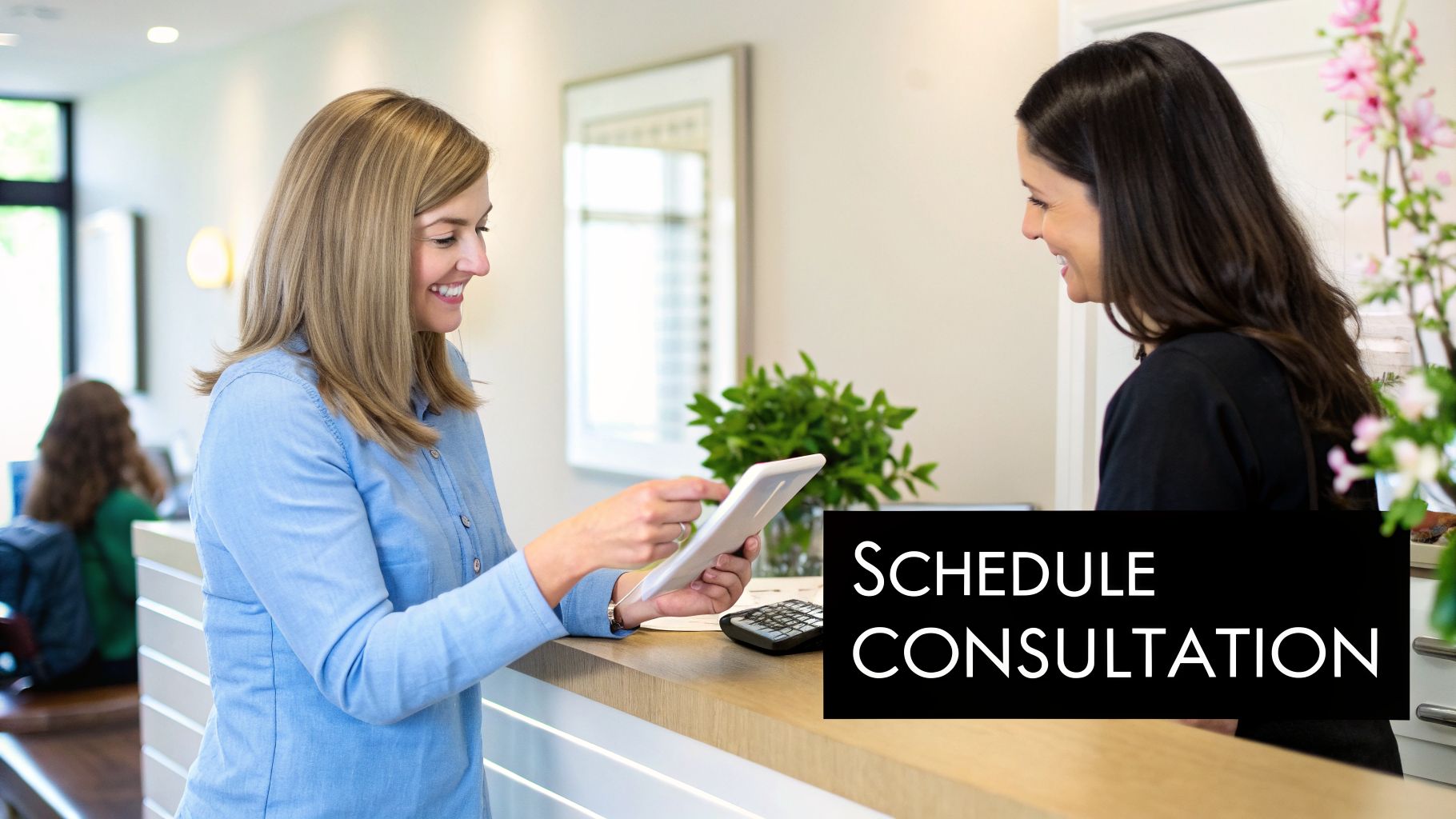 Two smiling women interact at a dental office reception desk, scheduling a consultation on a tablet.