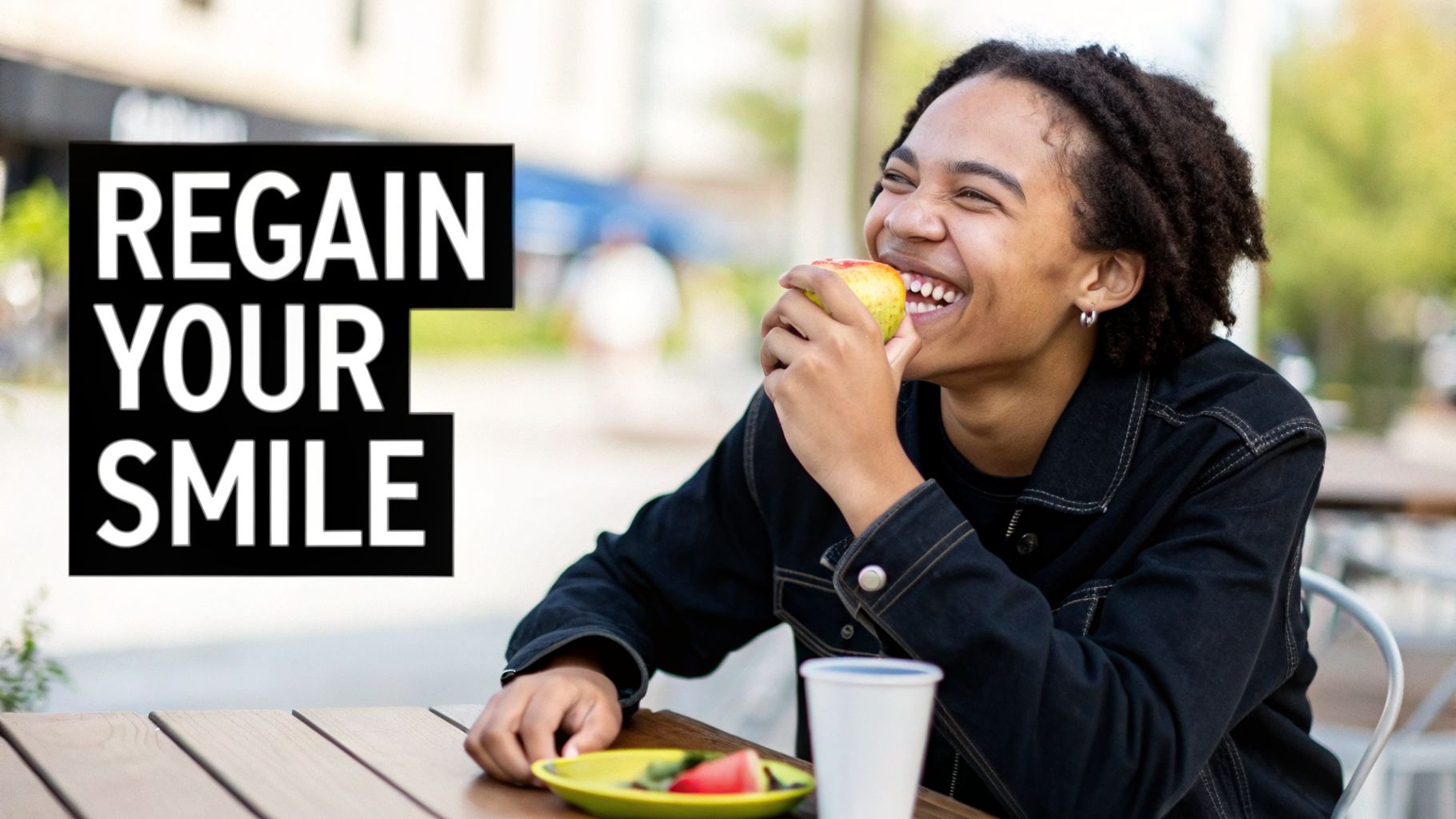 A happy person with curly hair smiles while biting into an apple at an outdoor table, with "REGAIN YOUR SMILE" text.