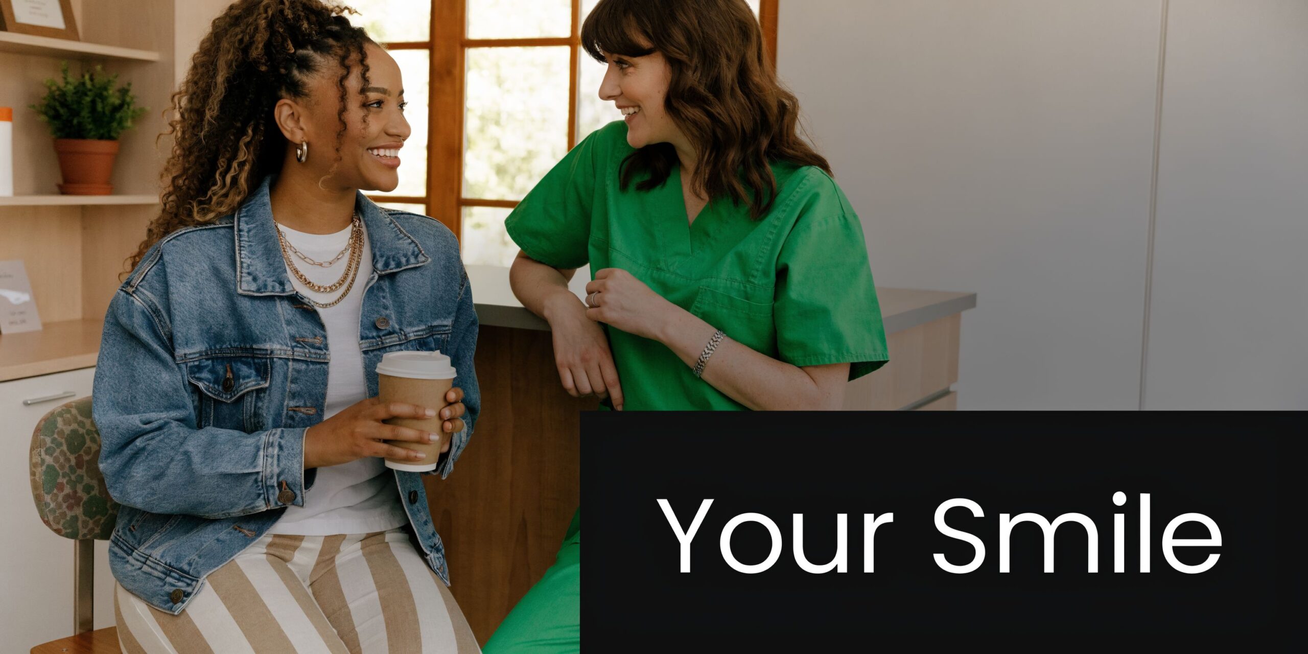 A smiling dental professional talking to a patient holding a coffee cup in a bright clinic office.