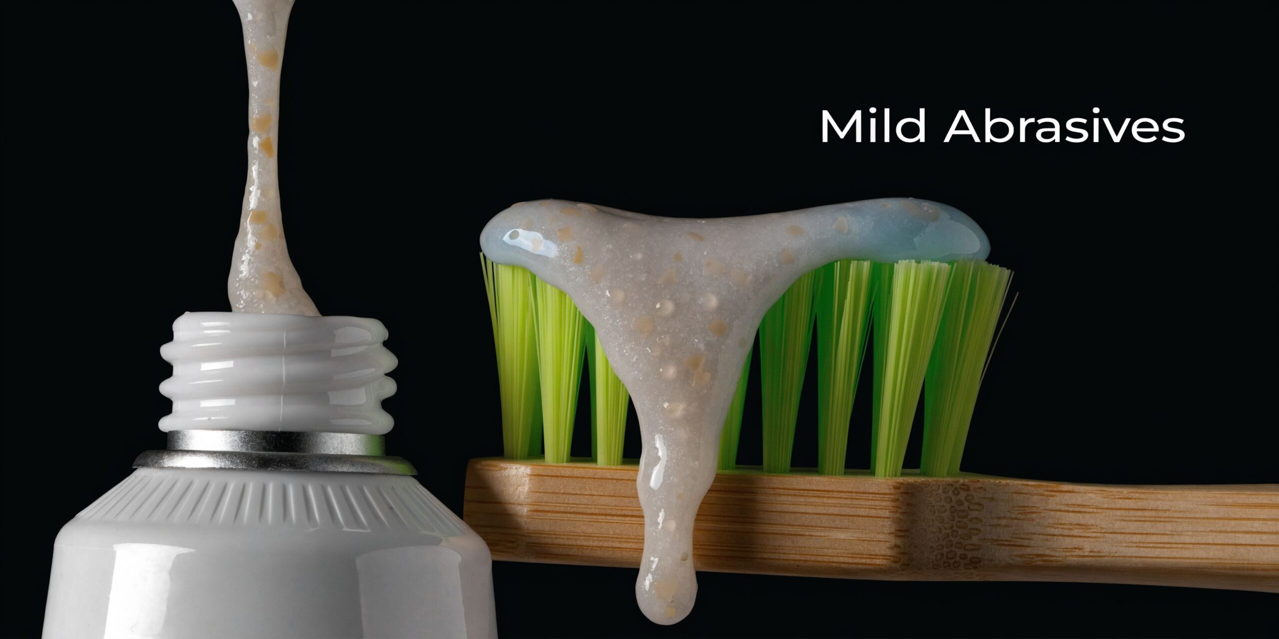 A toothbrush with toothpaste containing mild abrasives placed on top, with a tube of paste nearby.