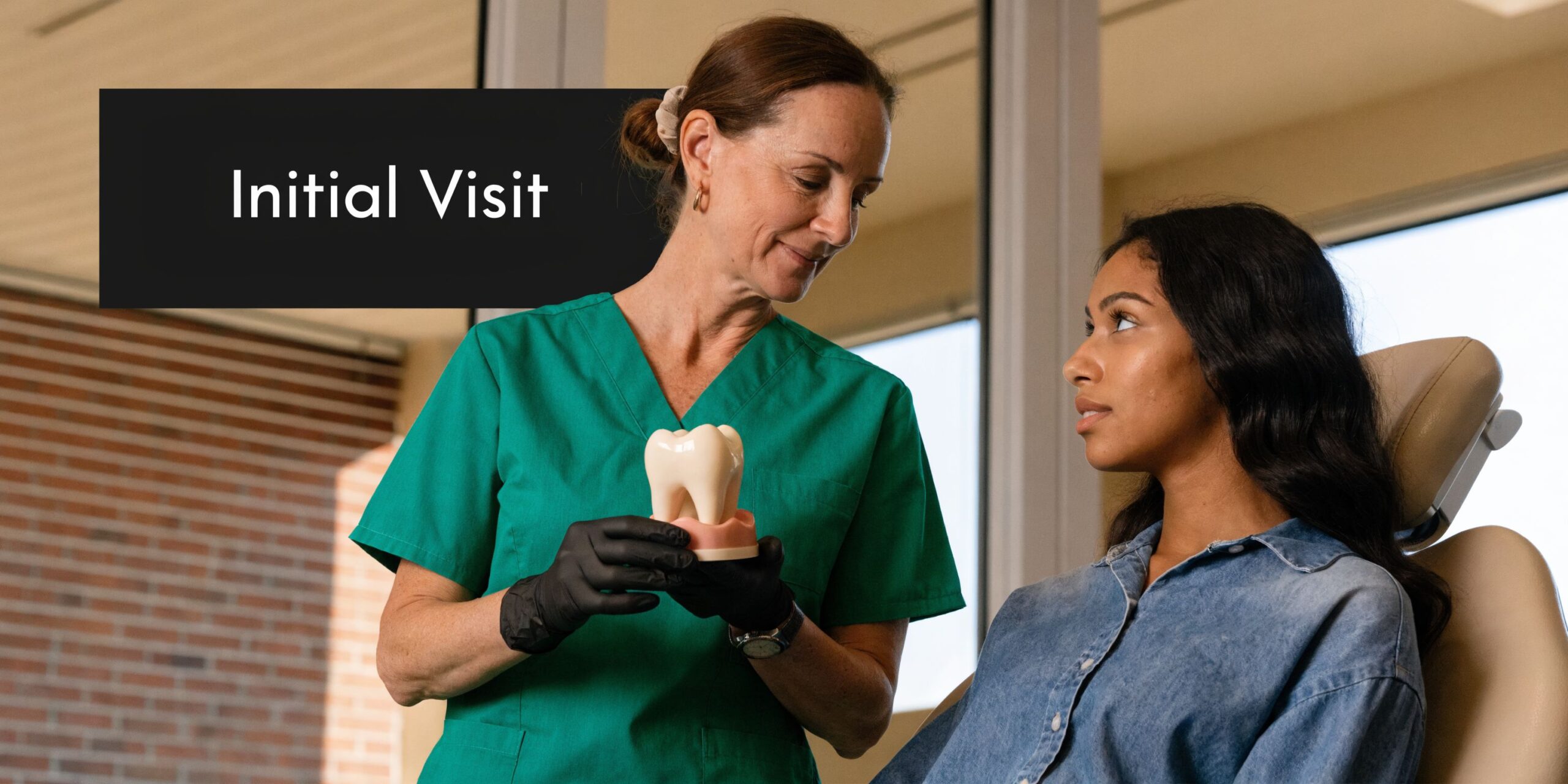A dentist wearing black gloves explains a dental crown procedure to a young patient in her office.