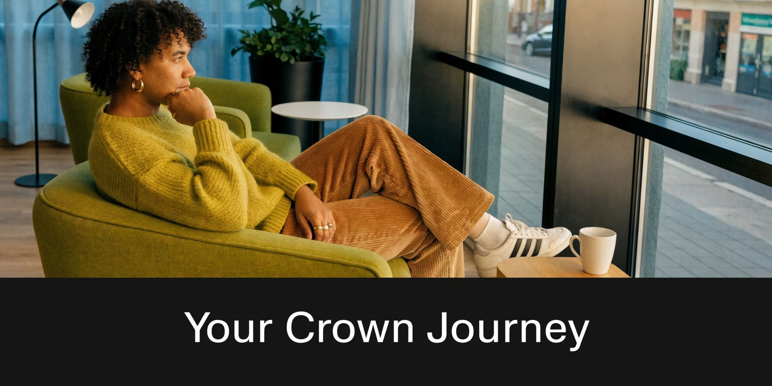 A person with curly hair wearing a yellow sweater relaxing in a green chair by a window.