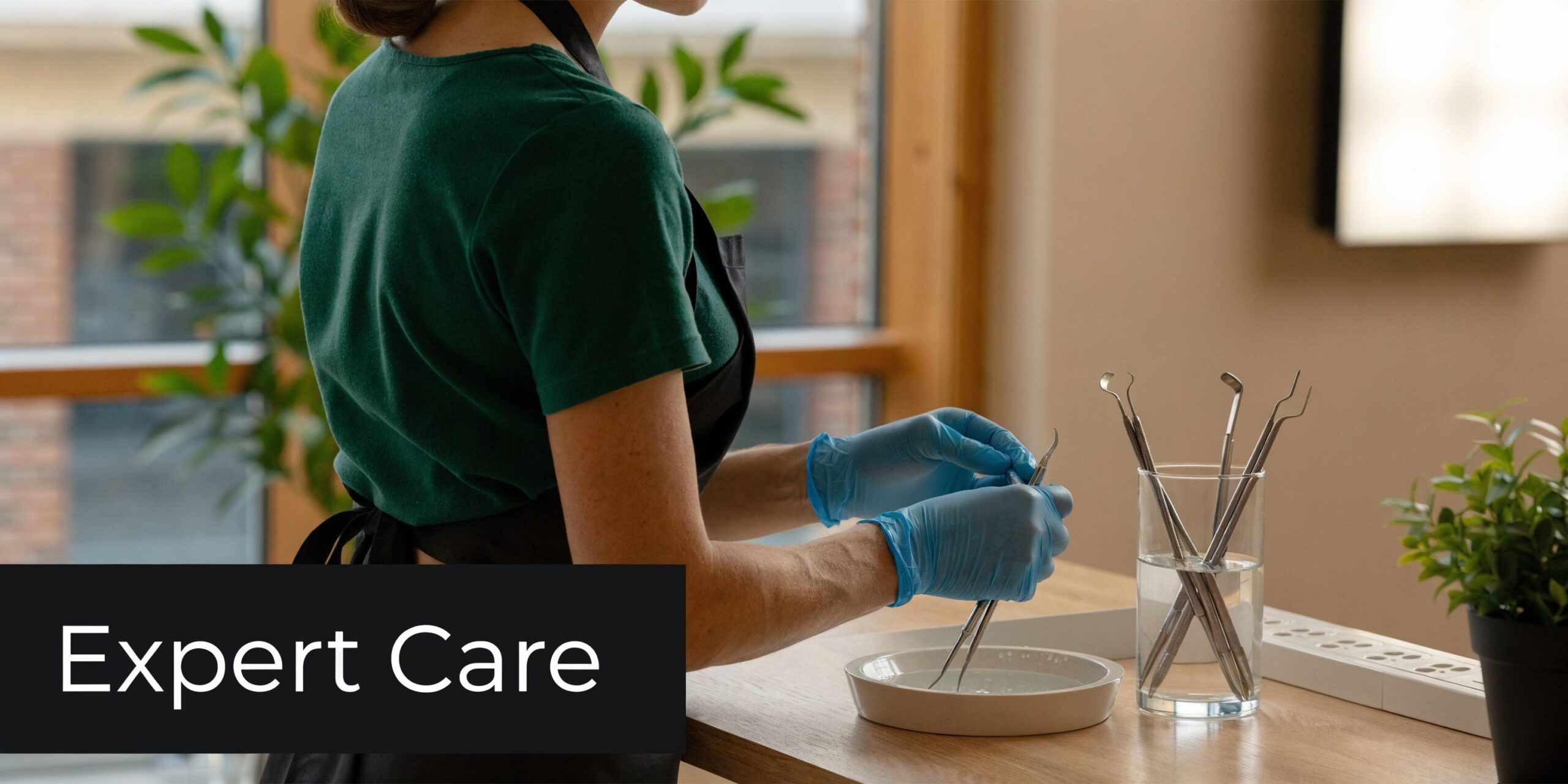 Dental professional wearing blue gloves cleaning specialized dental instruments in a clinic setting with natural light.